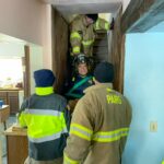 A group of firefighters practicing lifting another firefighter sitting in a rescue chair up the stairs of the training house.