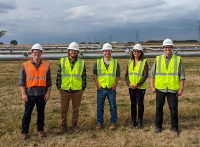 WEC Real Estate Team standing in a field wearing hard hats and reflective vests